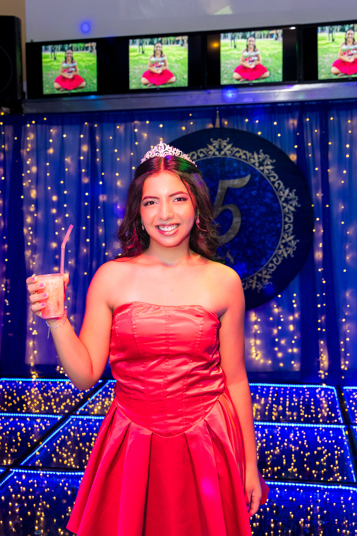 A debutante celebra seus 15 anos com um sorriso radiante, brindando na pista iluminada e transmitindo toda a alegria da noite.