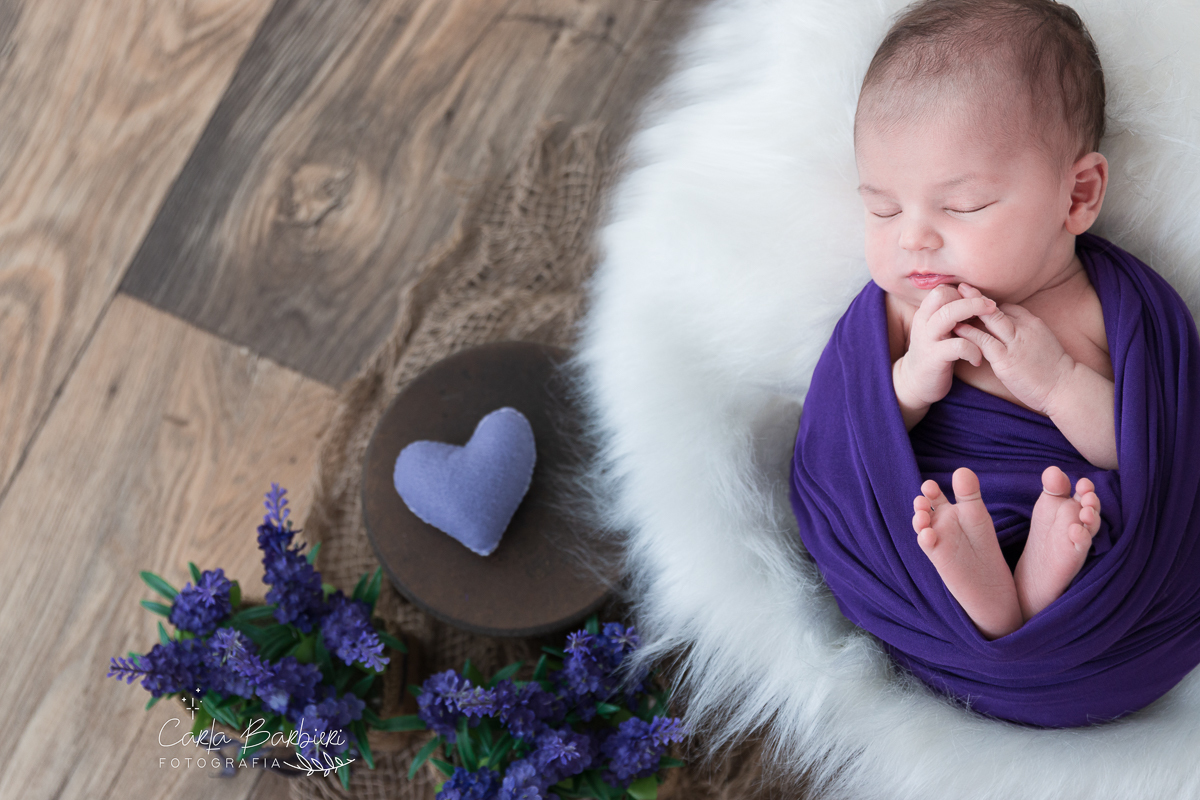 Júlia enrolada em wrap roxo com produção em pele, banquinho, flores e coração de enfeite.