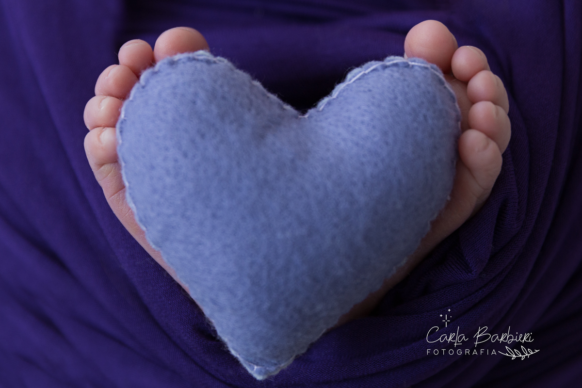 Foto detalhe do pezinho da Júlia segurando um coração de feltro roxo.
