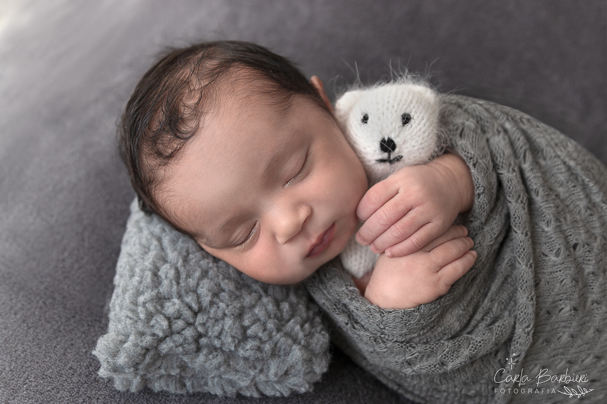 Fotografia de corte do Davi enrolado em wrap cinza em manta cinza com travesseirinho e mini toy de ursinho