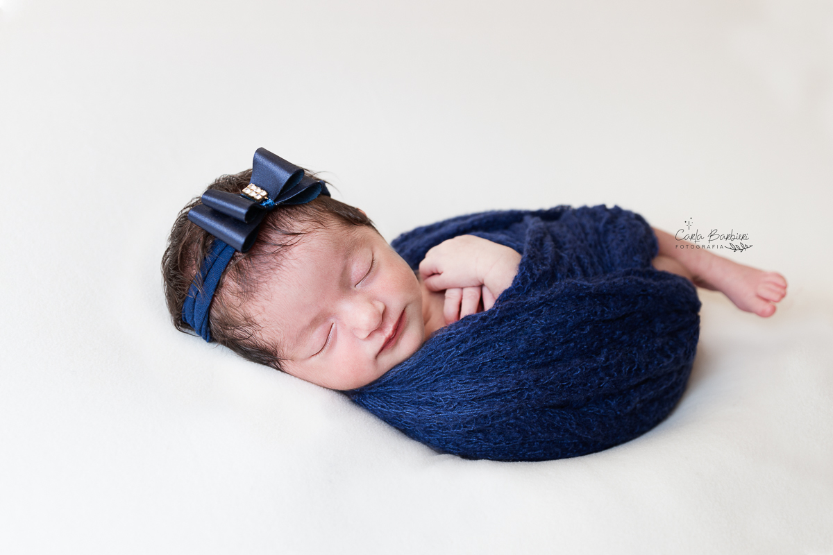 fotografia frontal da recém-nascida Rafaela enrolada em wrap azul marinho com headband de mesma cor
