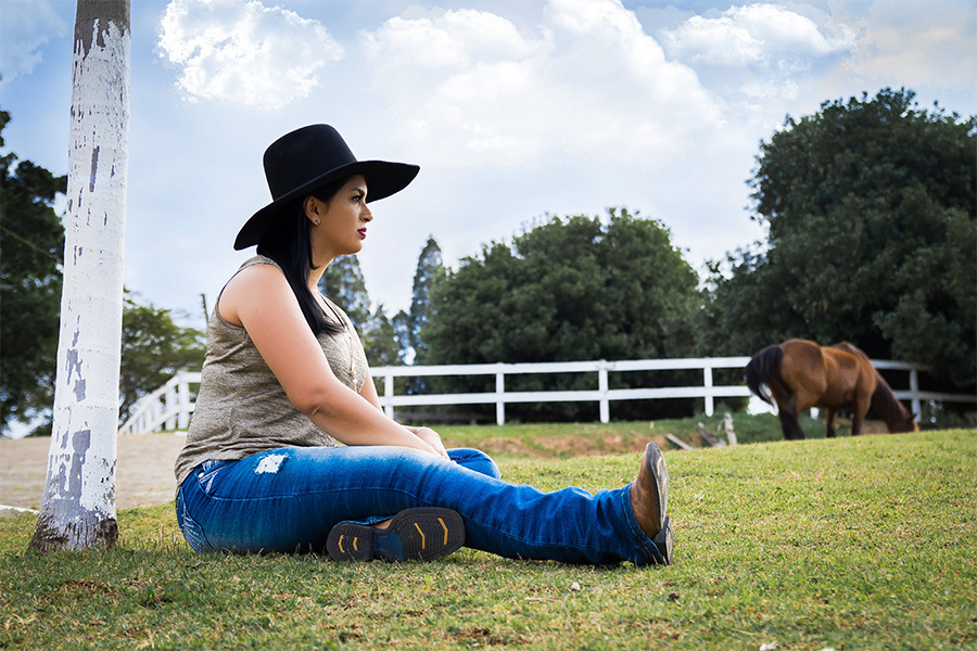 Sentada na grama e cavalos ao fundo