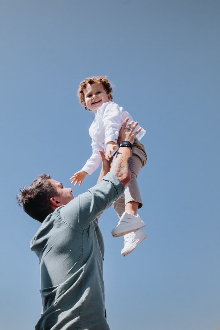 criança olha para foto sorrindo enquanto é erguida por seu pai no cristi redentor