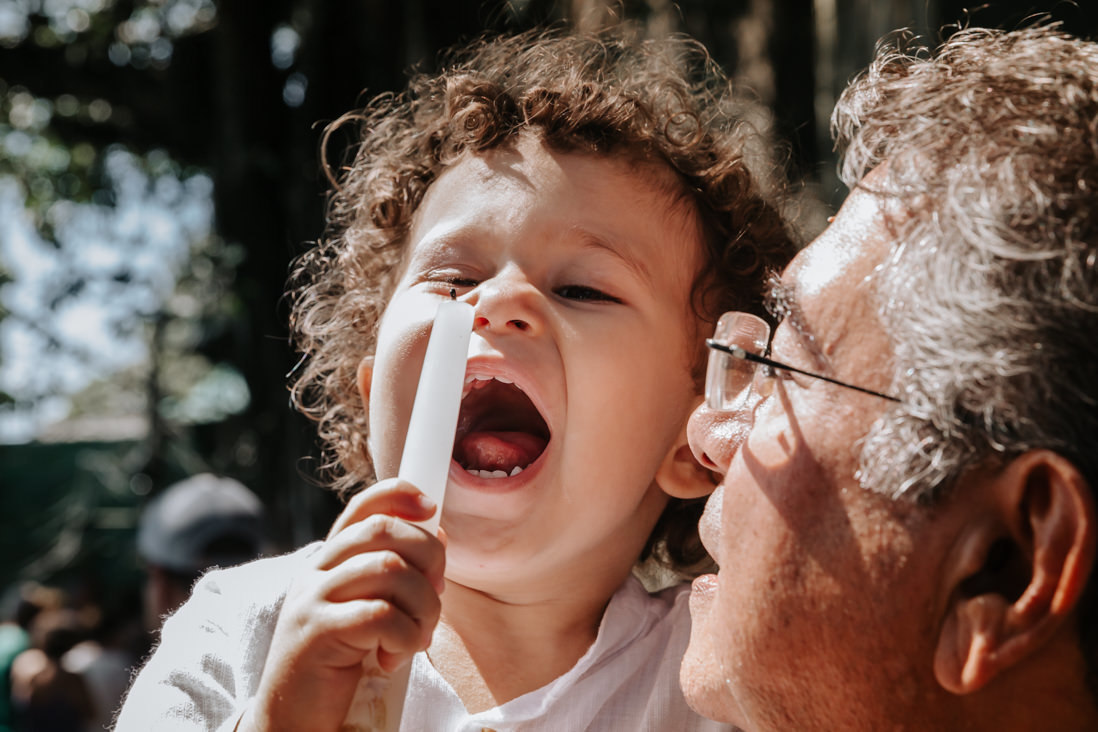 menino após batismo brinca com a vela do batizado sorrindo 