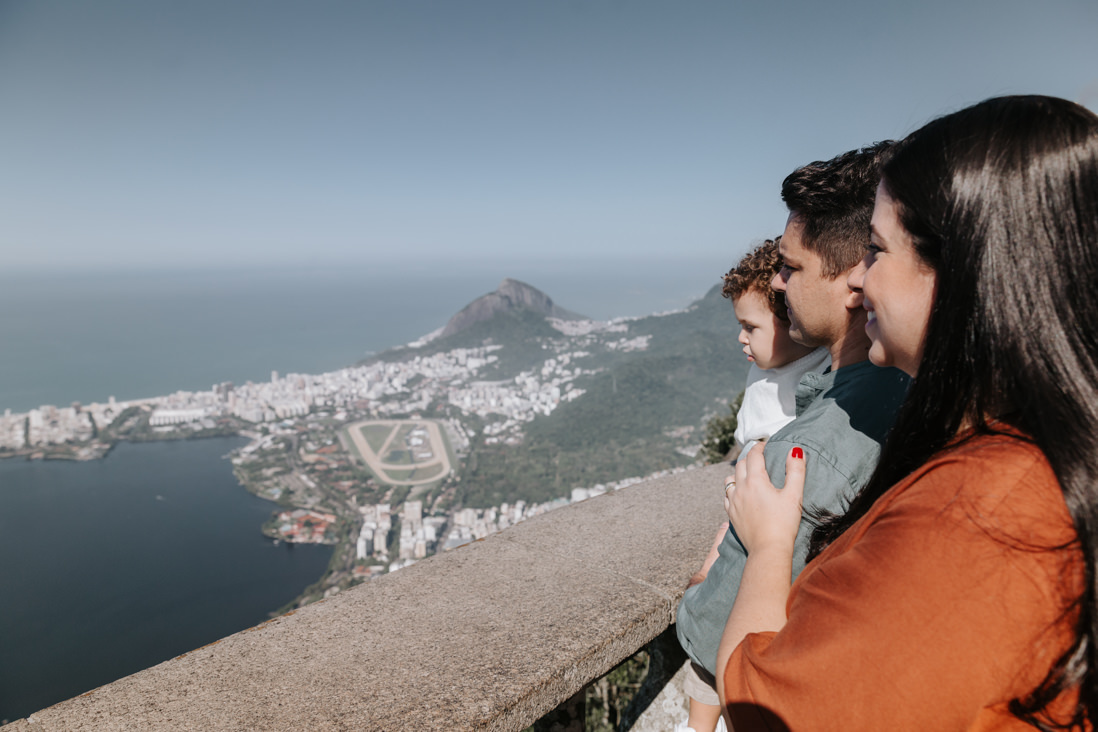 mae, pai e filho olham para a baía de guanabara do alto do cristo redentor no dia do batizado do gustavo