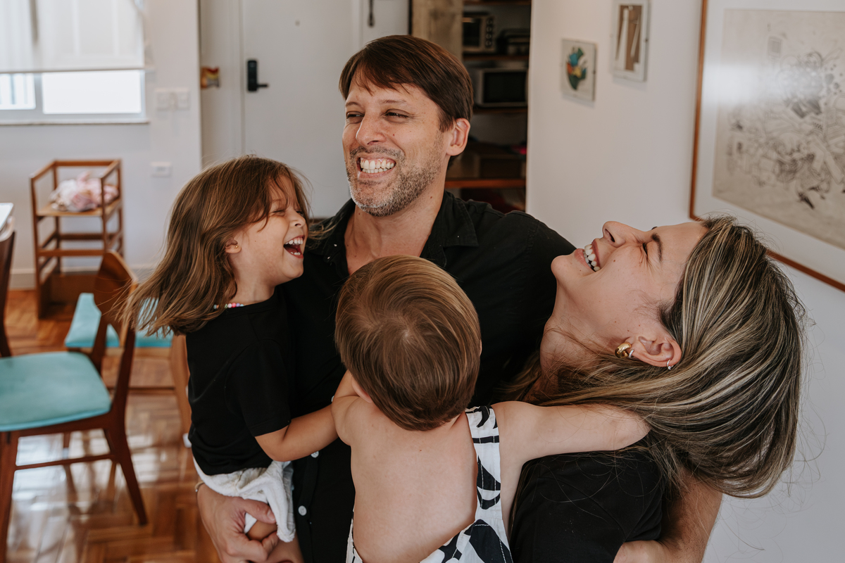 foto de uma familia brincando de rodar na sala de casa, o pai segura a filha mais velha e a mãe segura o filho mais novo, todos sorriem