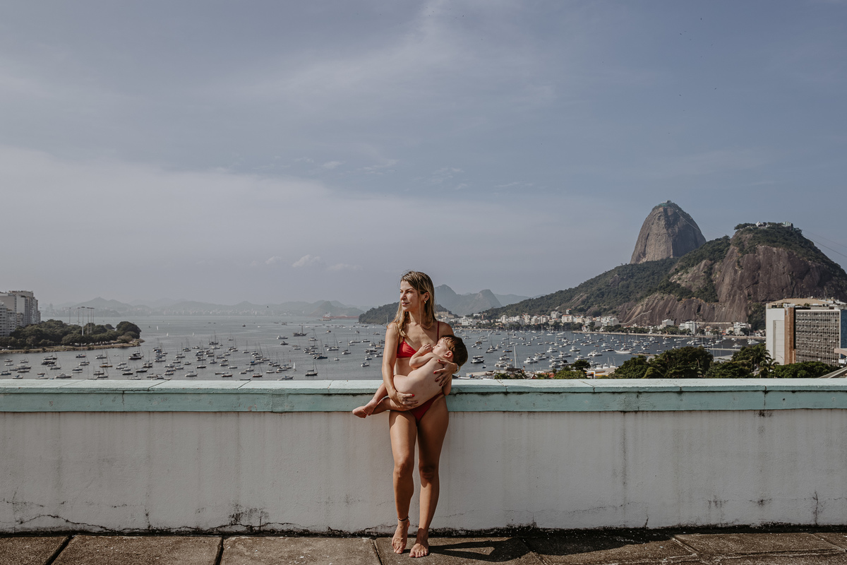foto da mae amamentando seu filho nu no terraço do predio ao fundo o bondinho do pão de açucar