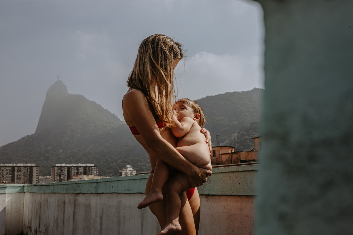 foto da mae amamentando seu filho nu no terraço do predio ao fundo o morro do corcovado no RJ
