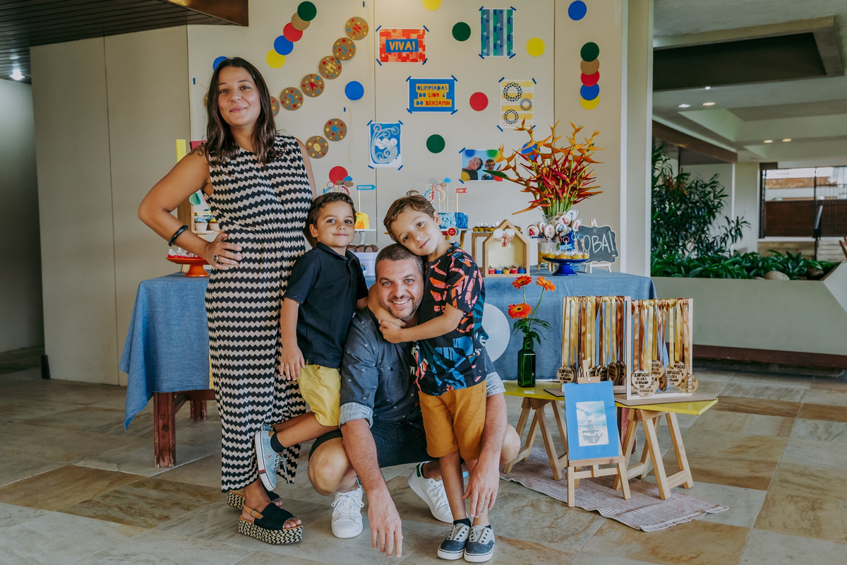Fotografia da família na frente da mesa do bolo com tema olimpíadas