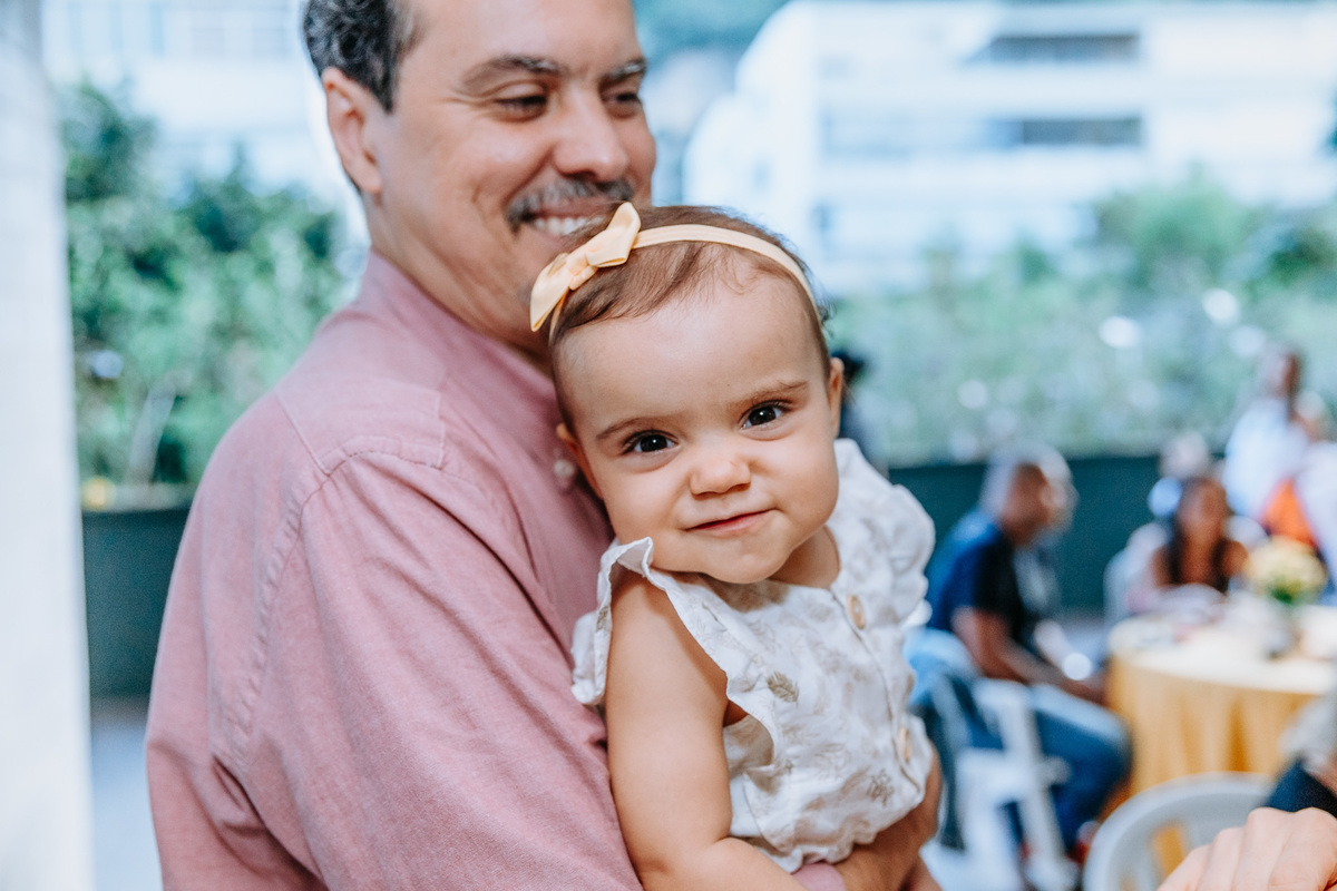 Fotografia de menina no colo do pai sorrindo pra câmera