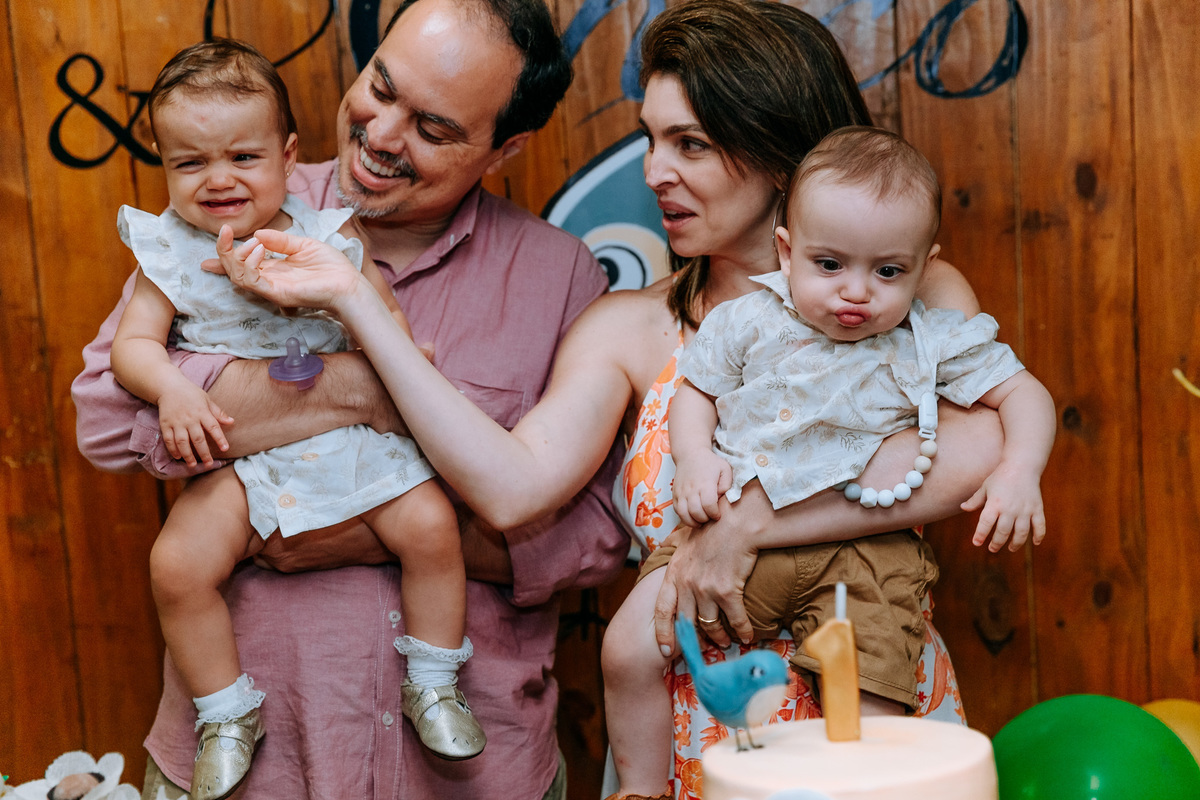 Fotografia dos pais com os gêmeos fazendo careta na mesa do bolo