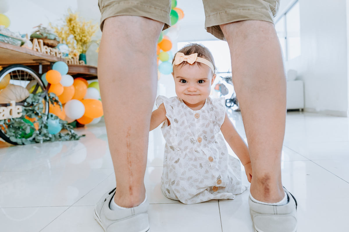 Fotografia de menina de 1 ano entre as pernas do seu pai na sua festa de aniversário entre as pernas do pai