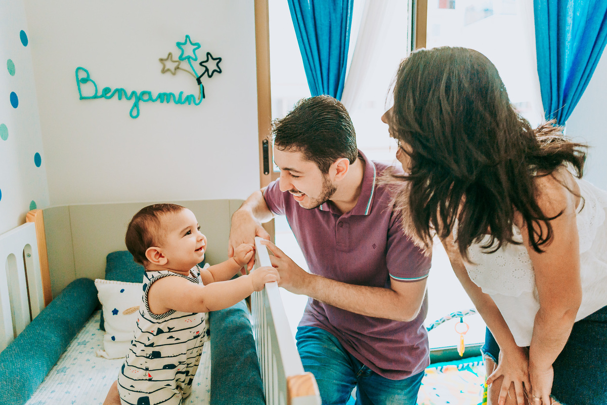 Fotografia de família lifestyle com os pais brincando com o bebê que está no berço