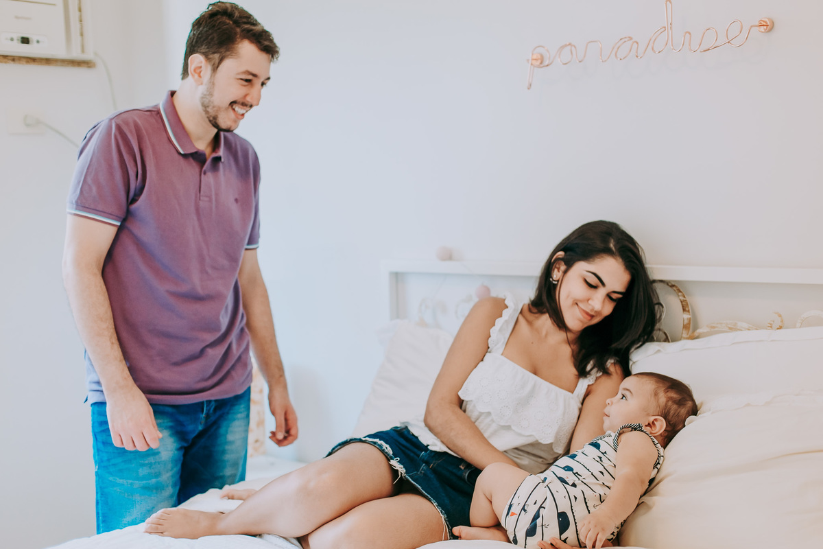 Fotografia de família com bebê admirando o pai e a mãe admirando o bebê