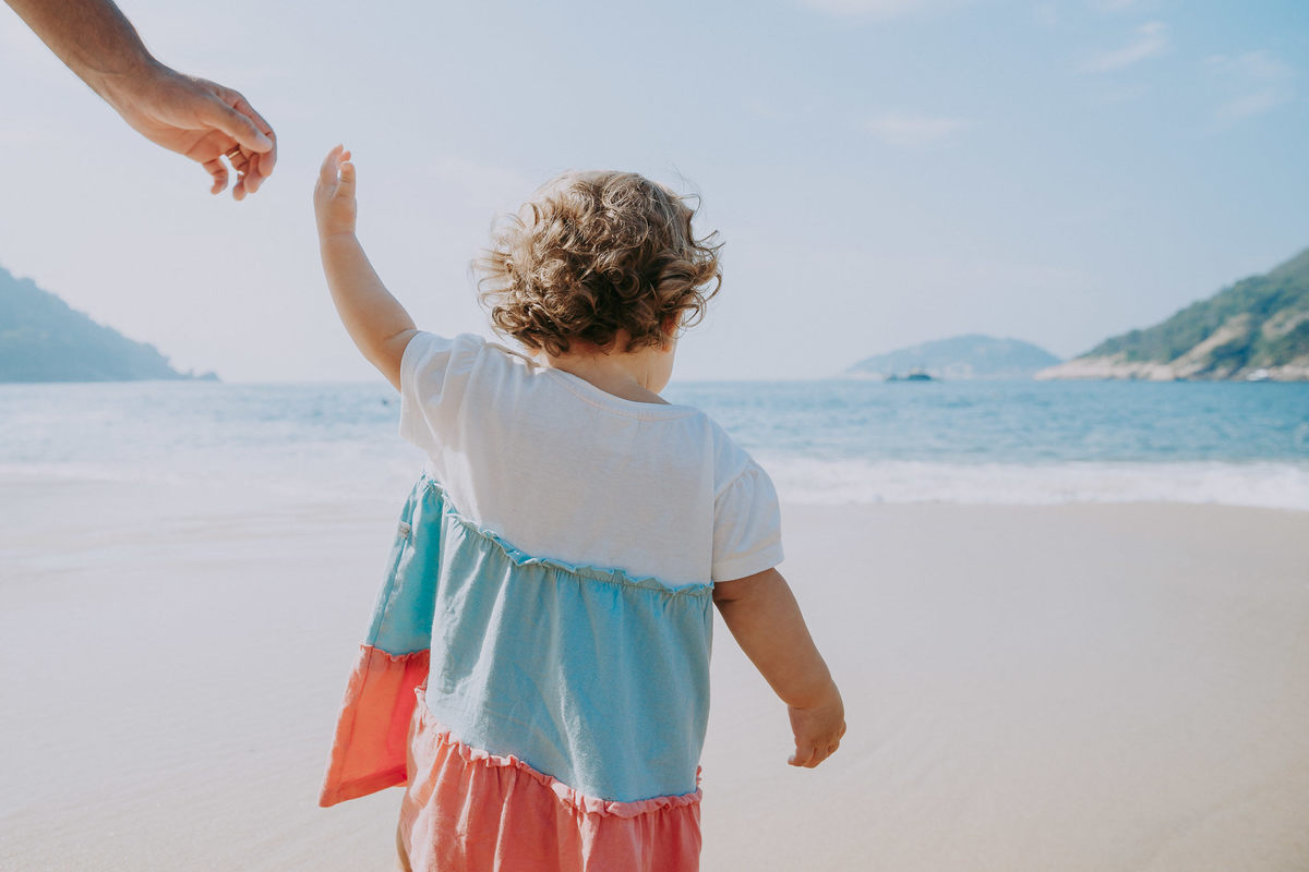Fotografia de menina de frente para o mar da praia vermelha soltando a mão do pai