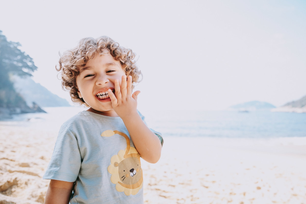 Fotografia de menino sorrindo para a câmera em frente ao mar da praia vermelha