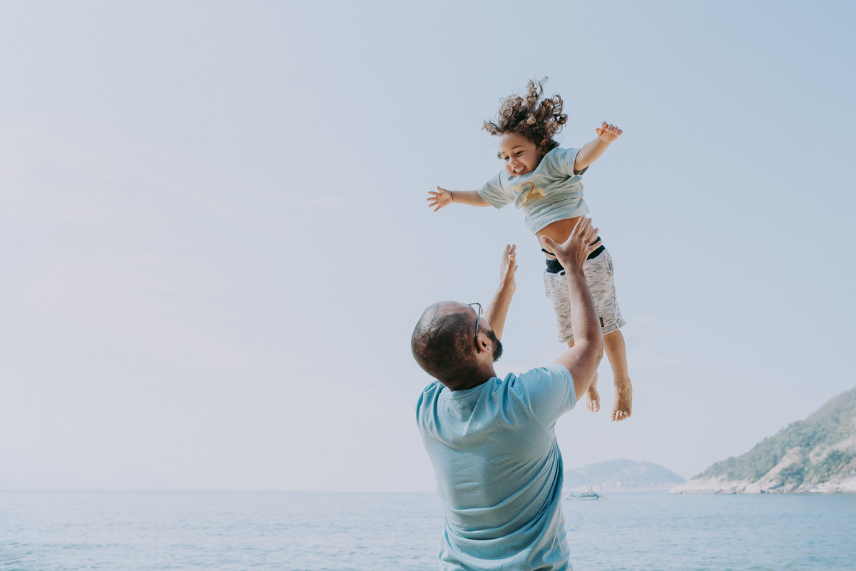 Fotografia de pai levantando o filho para o alto durante ensaio fotográfico de família na Praia Vermelha no RJ