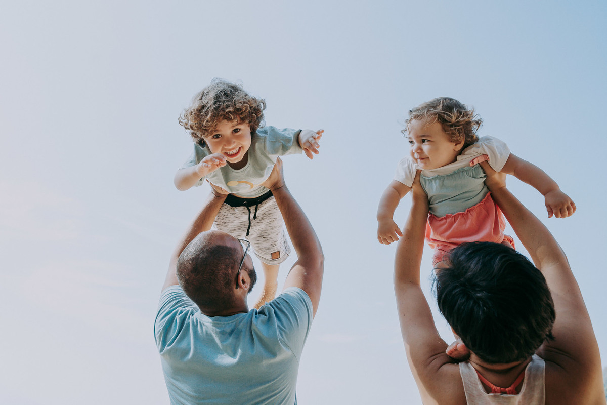 Fotografia de pai e mãe levantando os filhos para o alto durante ensaio fotográfico de família na Praia Vermelha no RJ