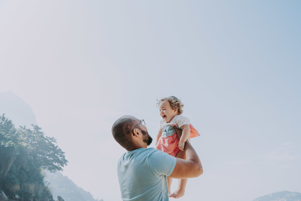 Fotografia de pai levantando a filha para o alto durante ensaio fotográfico de família na Praia Vermelha no RJ