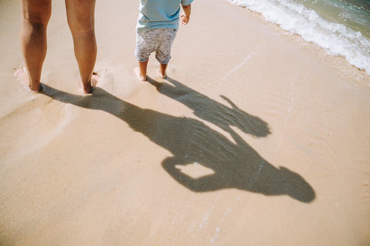Fotografia de sombra de mãe e filho com os pés na área da praia Vermelha no RJ durante ensaio fotográfico