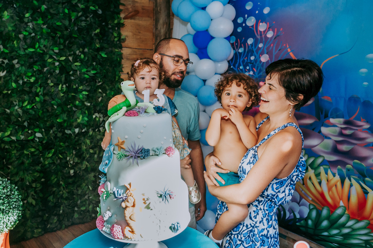 fotografia dos aniversariantes e dos pais sorrindo na mesa do bolo da festa infantil