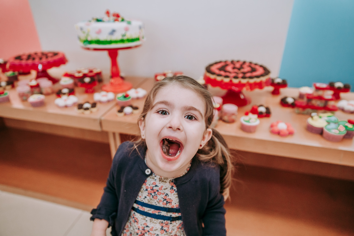 Fotografia de criança com a boca aberta cheia de brigadeiro em sua festa de aniversario na barra da tijuca