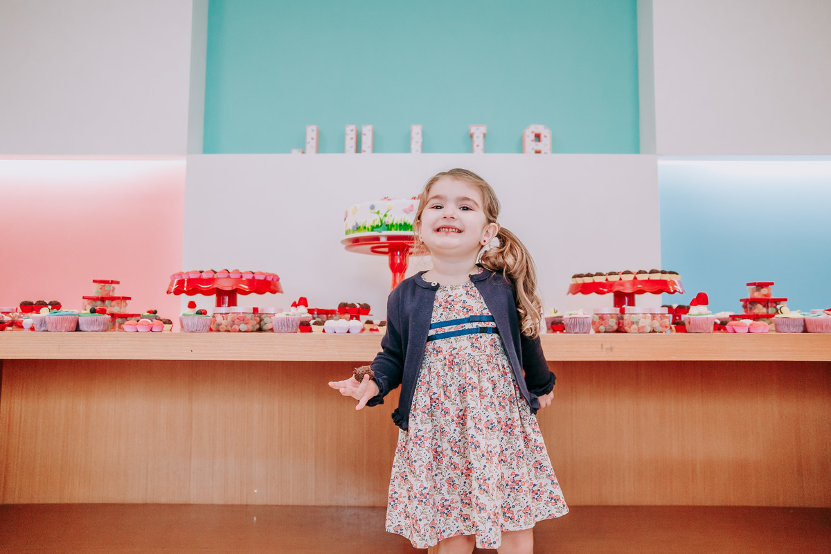 fotografia de criança sorrindo e segurando brigadeiro na mao direita em frente a mesa do bolo