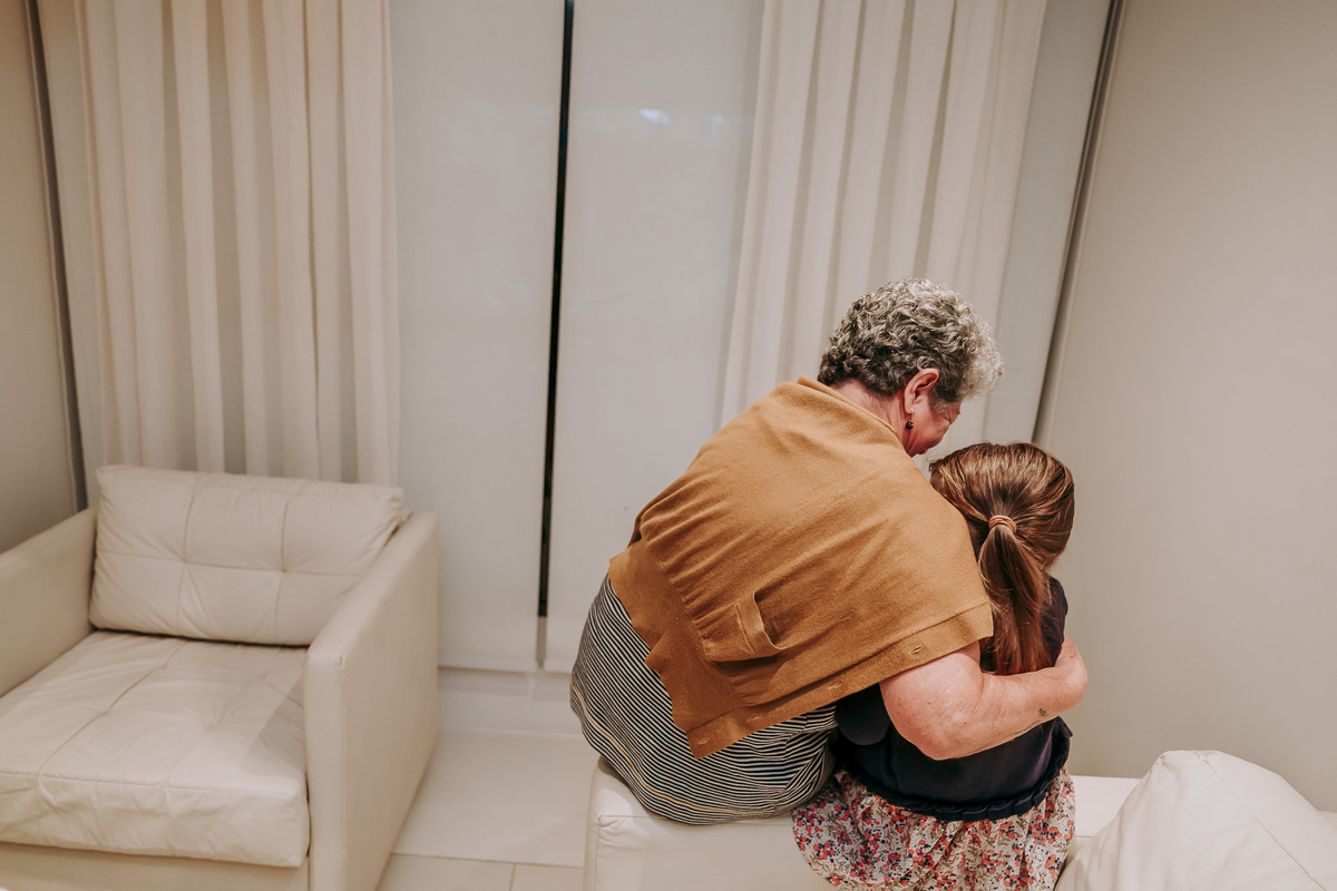 foto de neta e avó sentadas no braço de um sofa e ambas de costas para camera