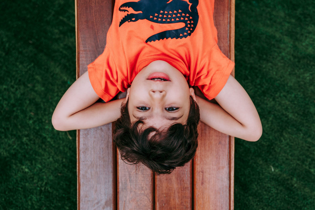 fotografia de menino deitado de blusa laranja olhando para o alto