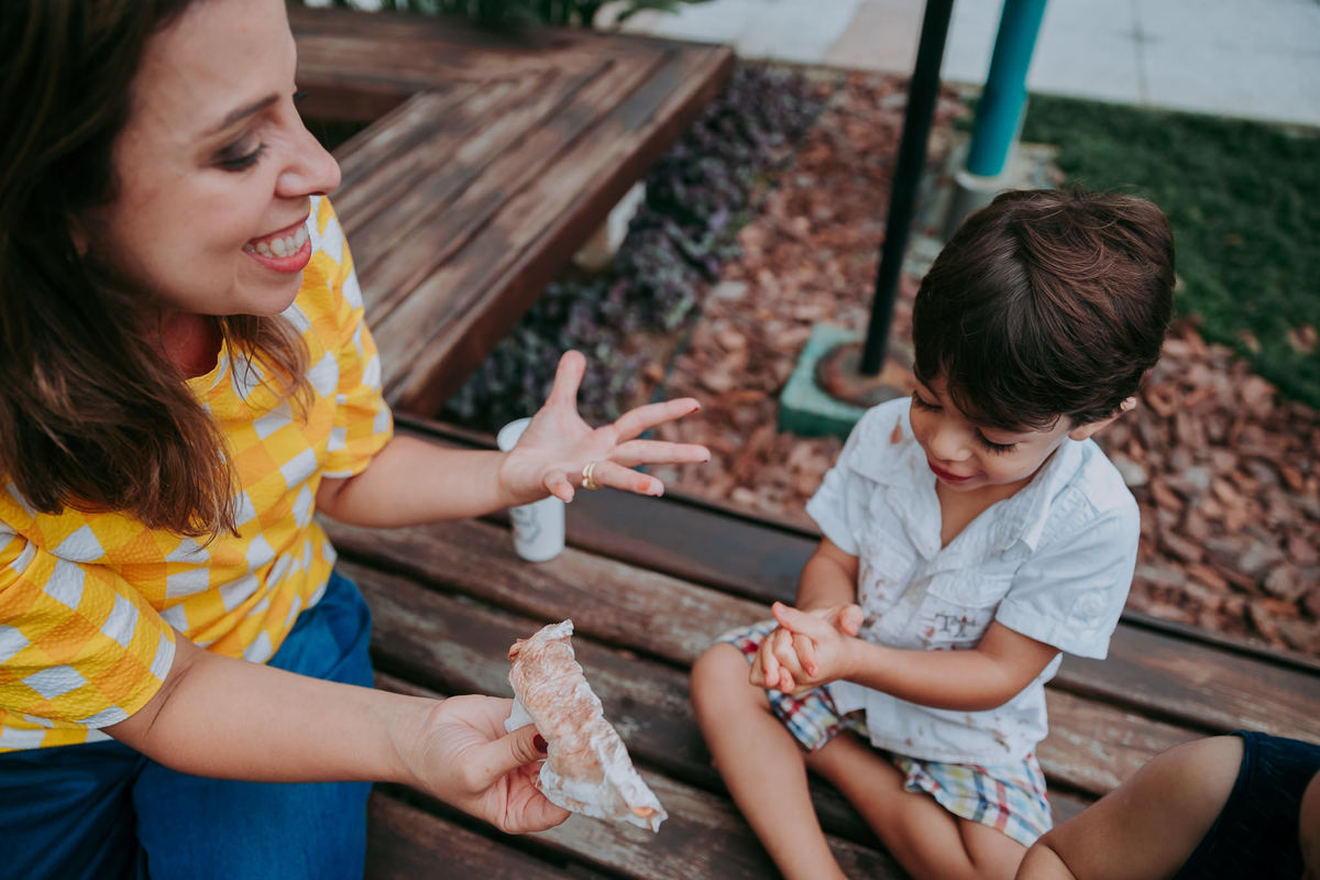 fotografia de mae sorrindo desesperada com o filho que se sujou todo tomando picole de chocolate