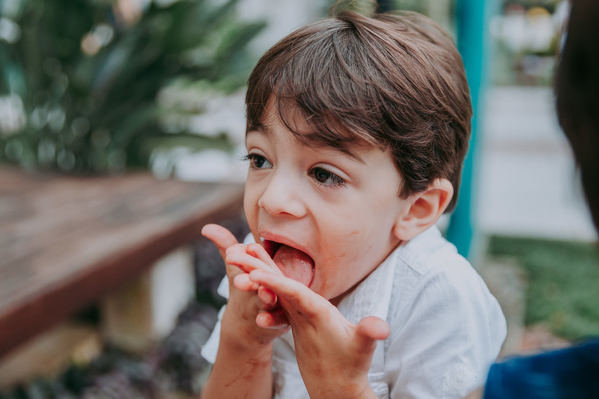 fotografia de menino lambendo a propria mao suja de sorvete de chocolate