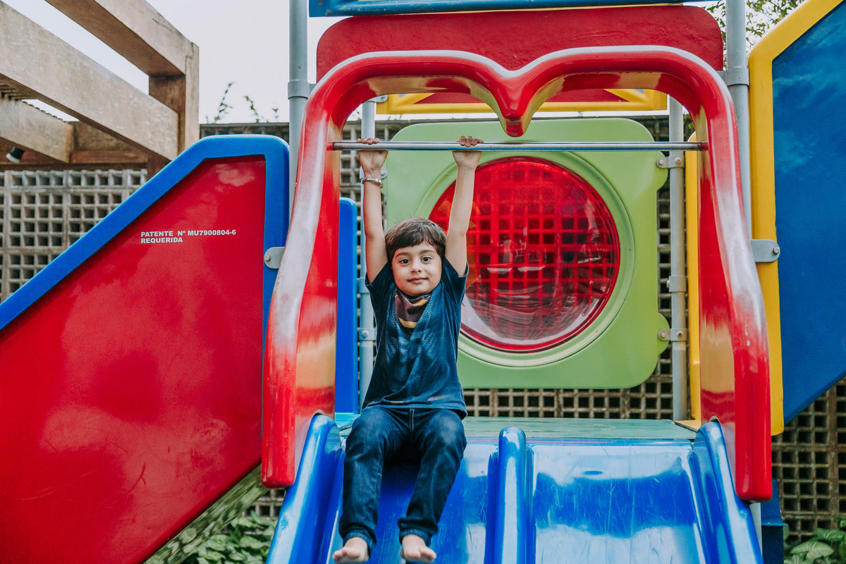 fotografia de menino pedurando em brinquero de escorrega colorido