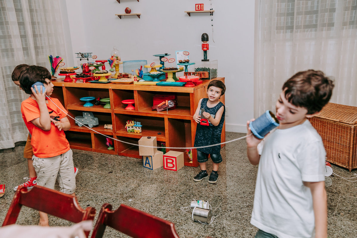 fotografia de dois meninos brincando de tefone sem fio enquanto sao observados por outro menino