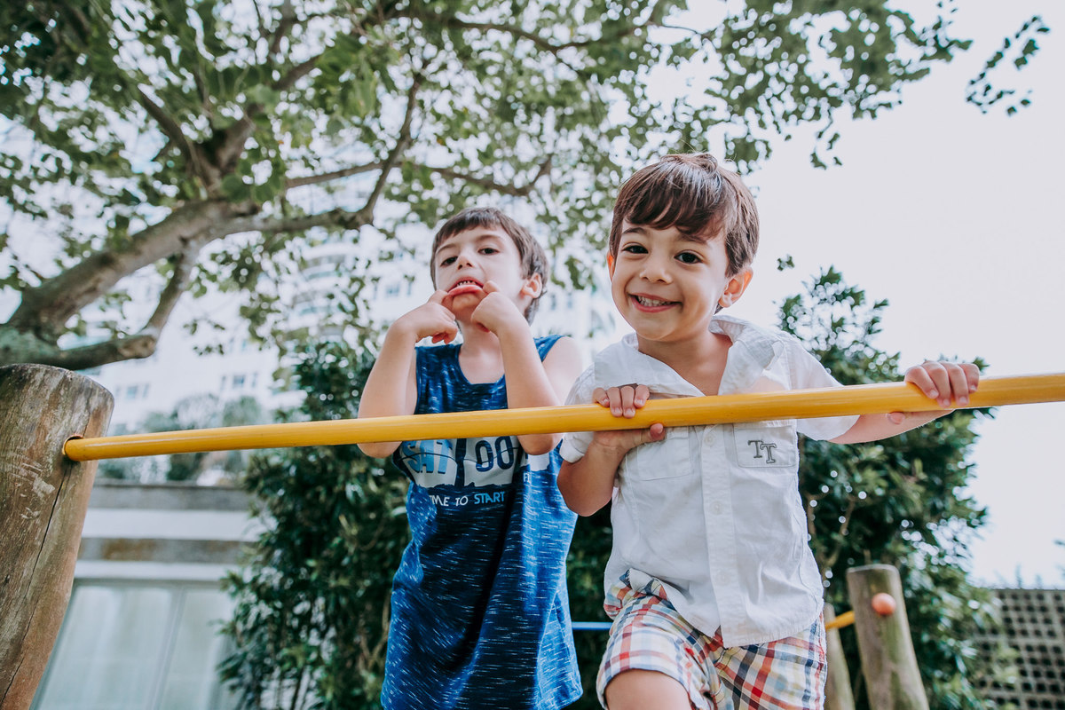 fotografia de dois meninos sobre um brinquedo de parquinho , um sorrindo e outro fazendo careta