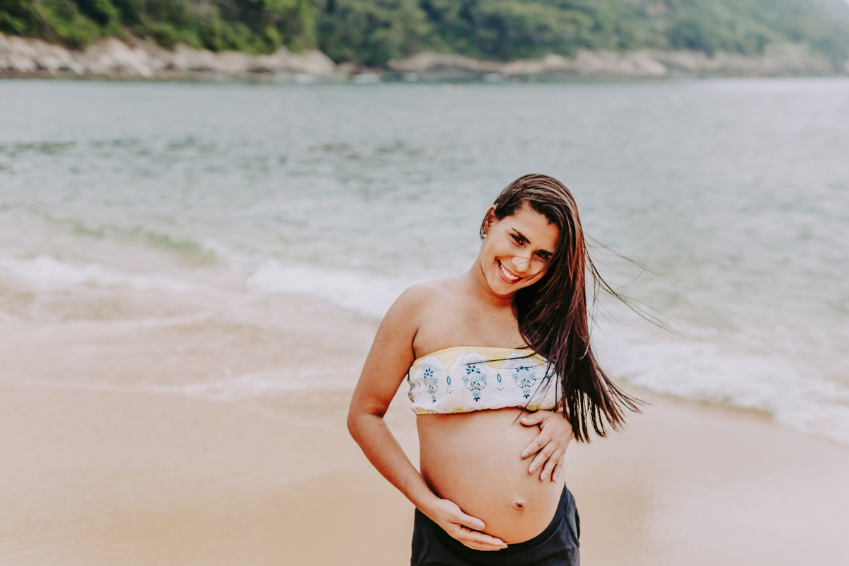 foto de meio corpo de gestante sorrindo para foto na praia