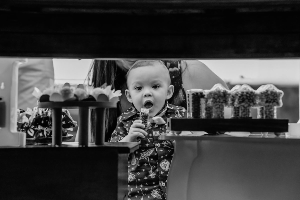 foto preto e branco de aniversariante atras da mesa do bolo  com objeto na boca