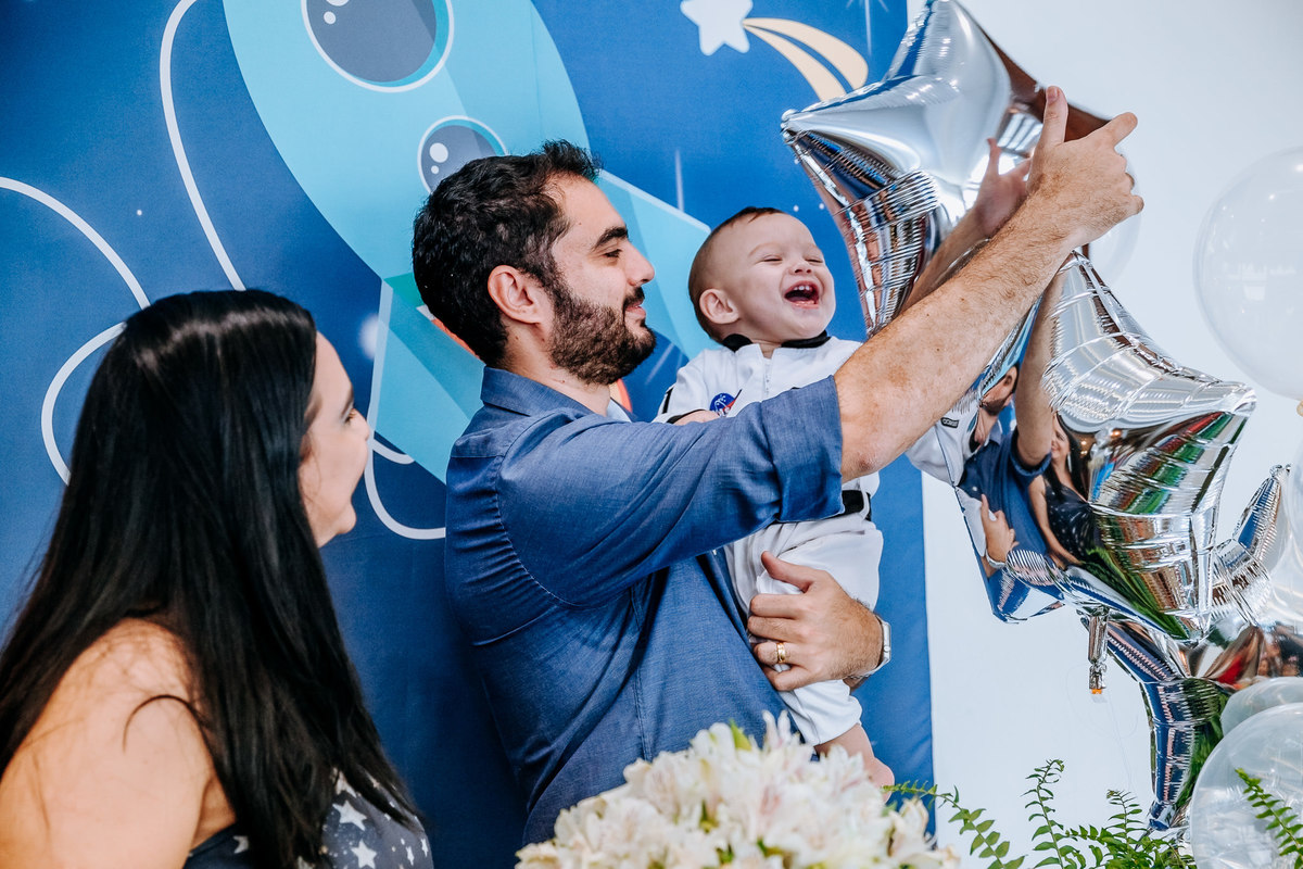 pai brinca com filho em reflexo de balão de gás hélio e mae observa