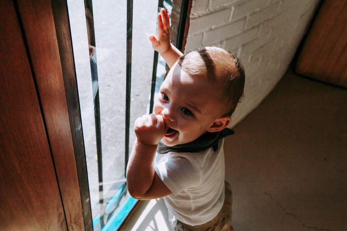 criança apoiada em porta com a mão na boca sorrindo para a camera