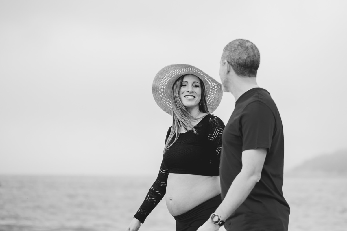 foto em preto e branco de casal caminhando pela praia, mulher de chau sorri pra ele e ela de frente pra câmera