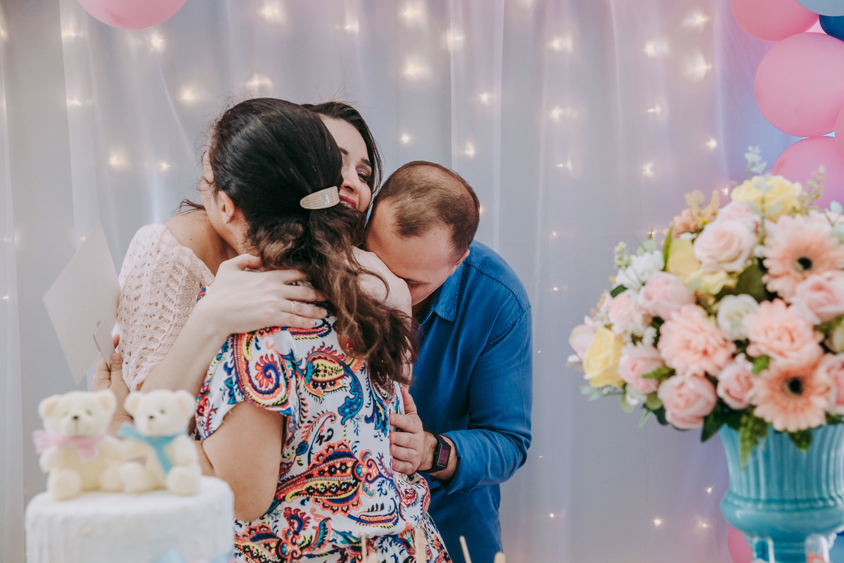 casal gestante abraça carinhosamente amiga na mesa do bolo do cha revelacao