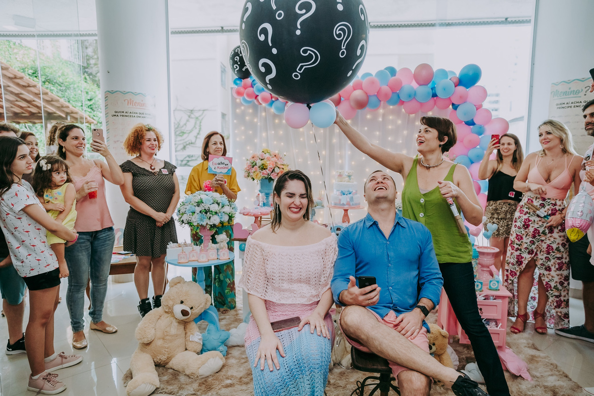 casal gestante apreensivos com o estouro do balão sobre suas cabeças em frete à mesa do bolo do chá revelação