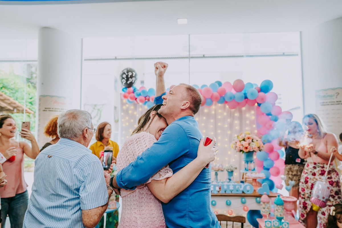 marido vibra com braço para o alto emocionado abraçado à esposa gestante no chá revelação após ver que teria filho menino