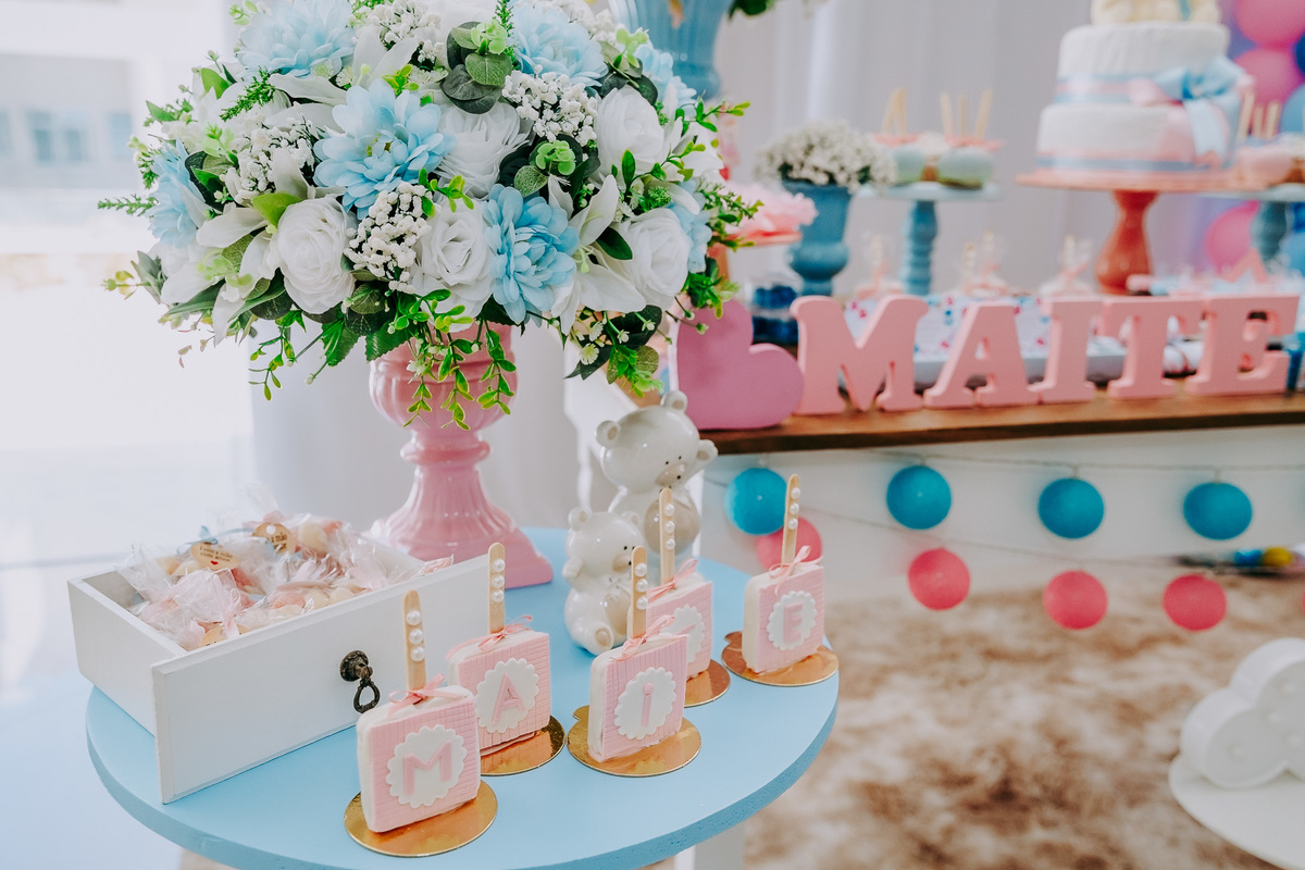detalhe de decoracao de chá revelacao pirulitos rosa sobre mesa com uma jarro de flores azul e branco
