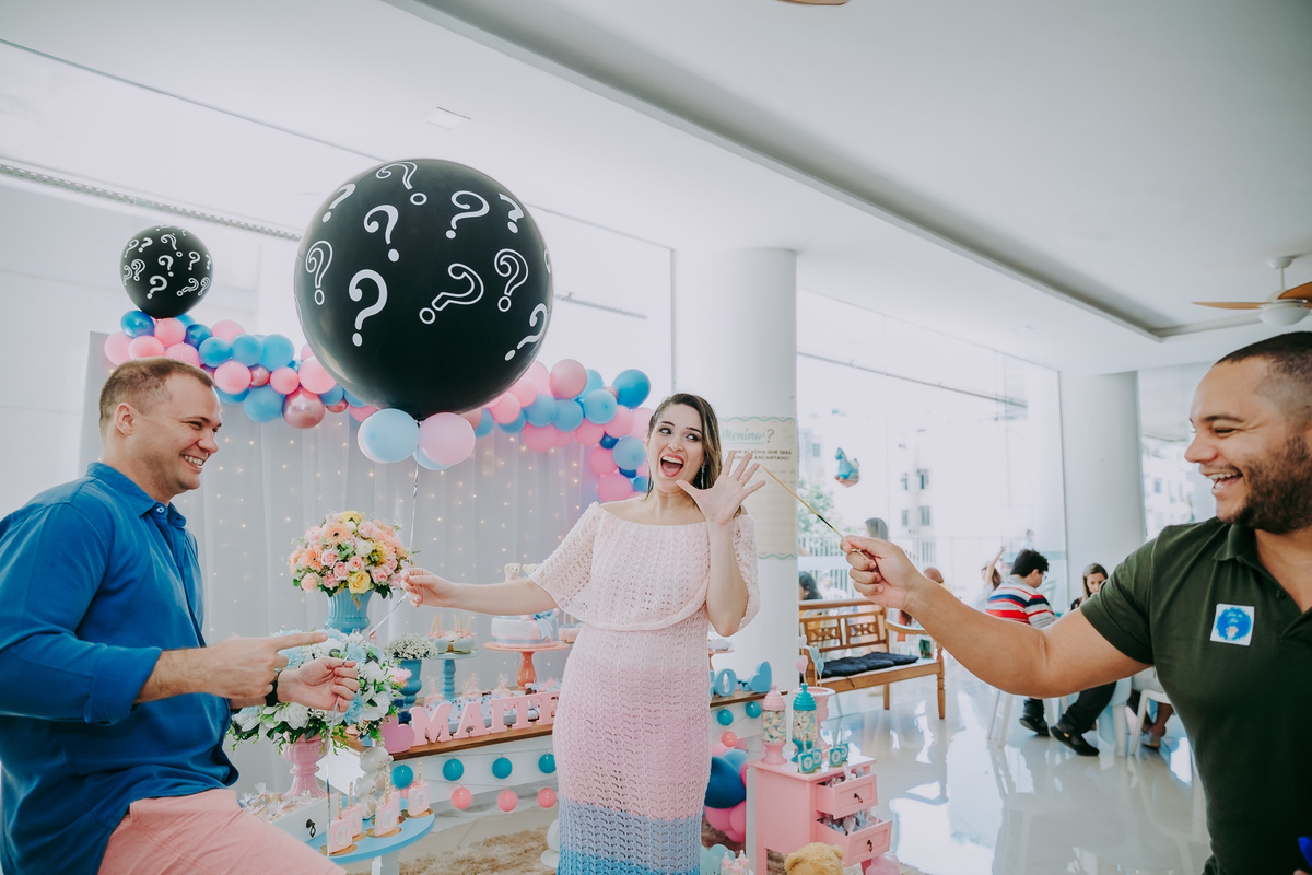 marido e gestante brincando com convidado enquanto ele  ameaça estourar o balão