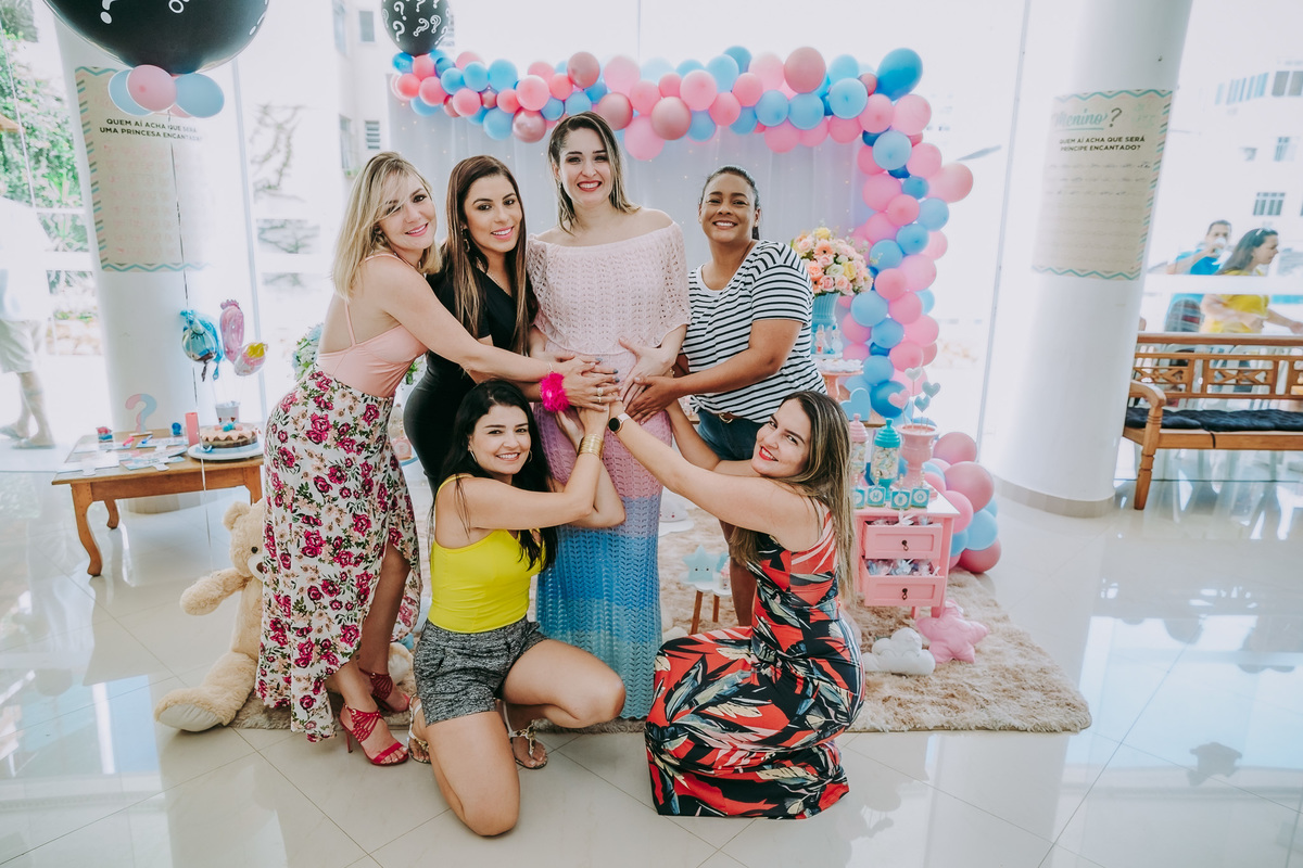 cinco amigas com a mão na barriga da gestante no chá revelacao em frente a mesa do bolo