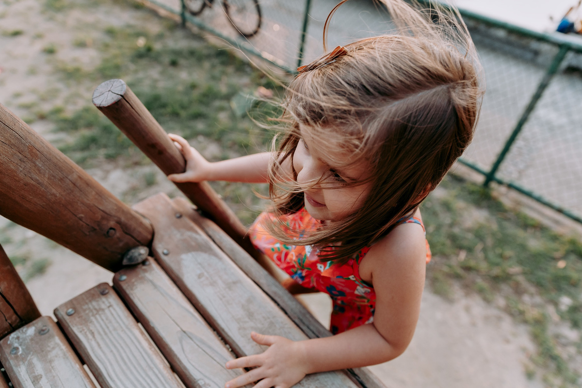menina de vestido vermelho sobe em escorrega em parquinho durante ensaio fotografico no rj