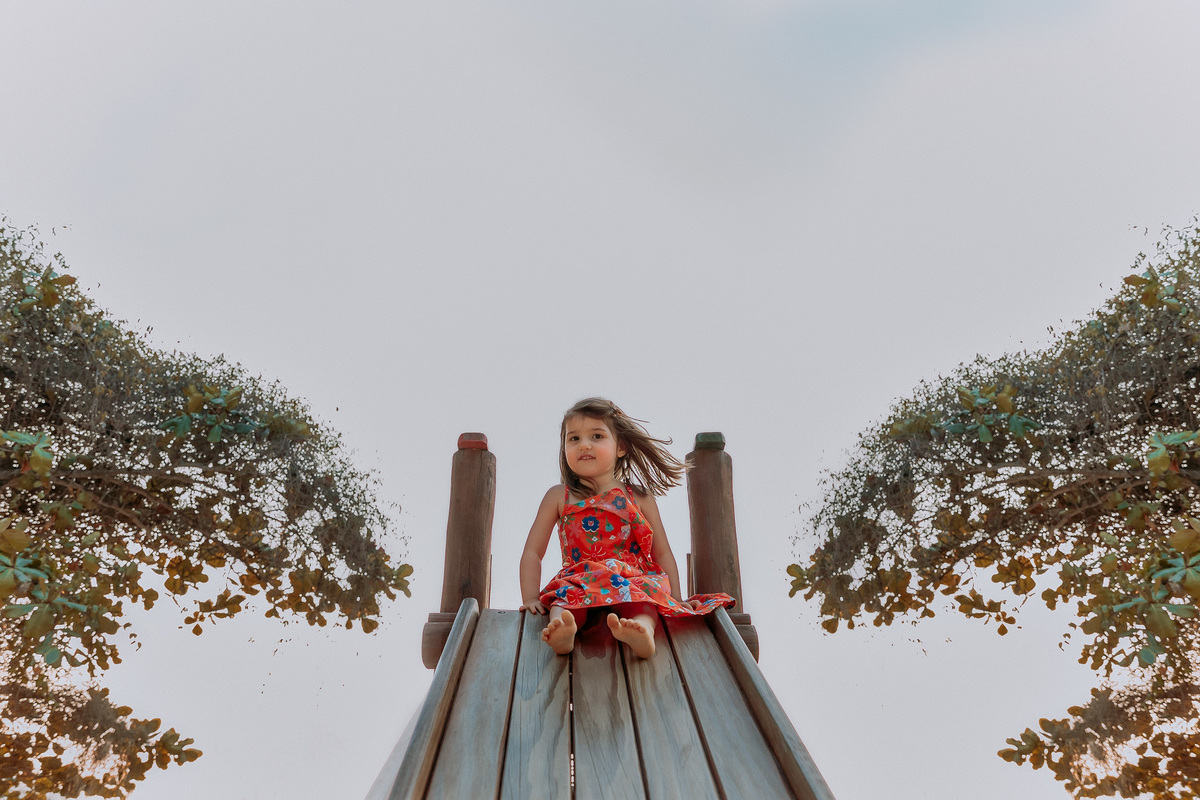 menina de vestido vermelho descendo de escorrega em parquinho no quadrado da Urca em ensaio familia realizado por crisb fotografia no rj