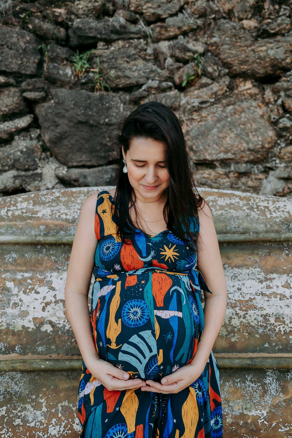 Gestante de vestido azul estampado encostada em barco na praia vermelha durante ensaio fotografico no rj