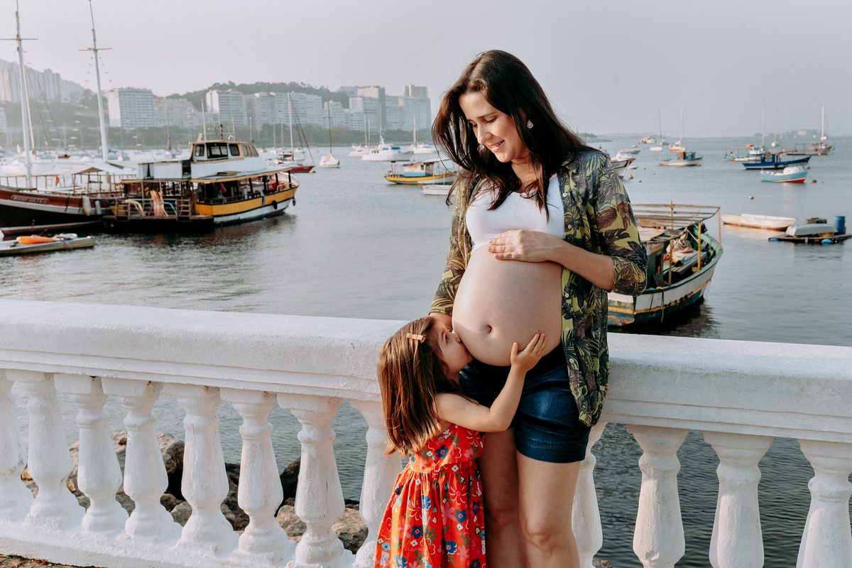 filha beija barriga da mae gestante enquanto olha em seus olhos, foto feita no quadrado da urca rj