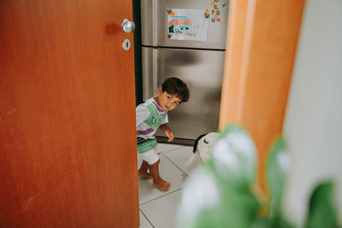 menino sorrindo abre porta da cozinha comendo brigadeiro